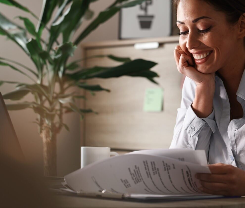 Young happy businesswoman reading reports while working in the o