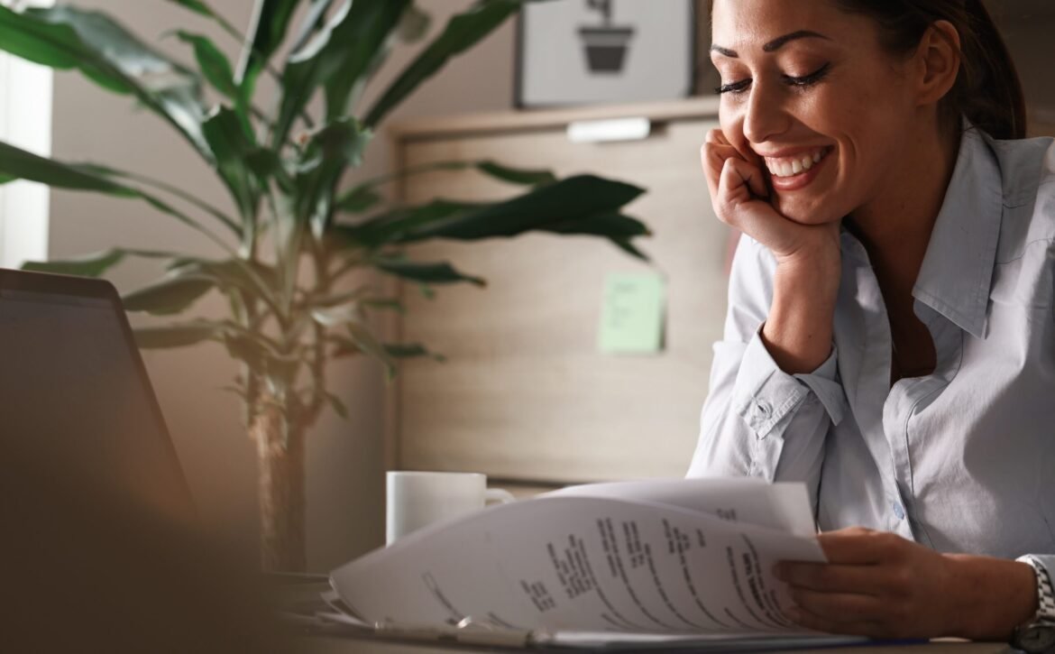 Young happy businesswoman reading reports while working in the o